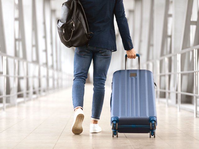 Person rolling suitcase in airport, seen from behind