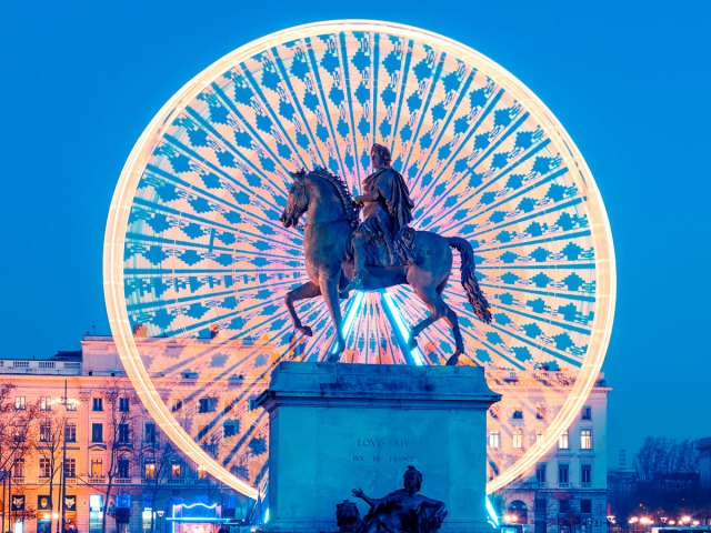 Statue of man riding horse and Ferris wheel decorated with holiday lights in Lyon, France