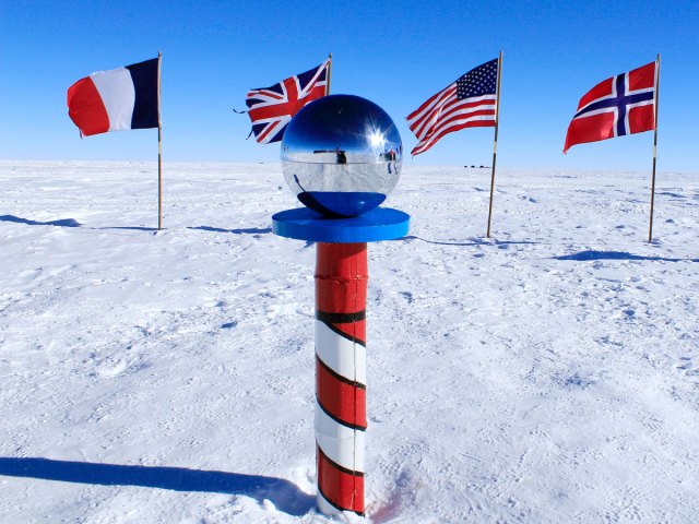 Ceremonial South Pole on icy landscape surrounded by national flags