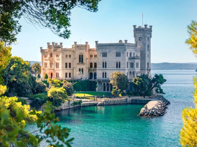 View of Italy's Castello di Miramare on peninsula, framed by trees