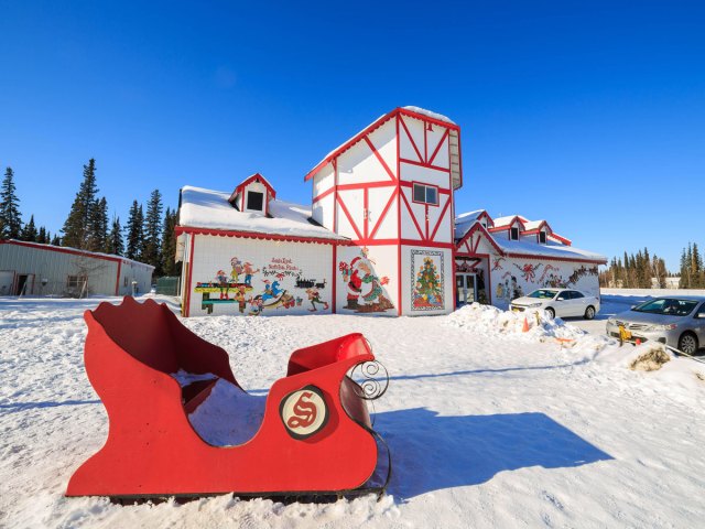 Red sled on snowy lawn and building adorned with Christmas decorations in North Pole, Alaska