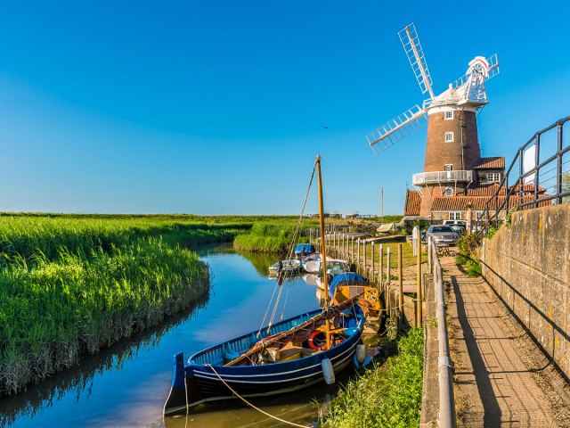 Windmill and boats docked in river in Cley-next-the-Sea, England