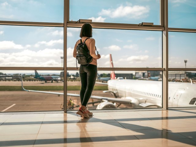 Airline passenger standing at window looking at airplane parked at gate