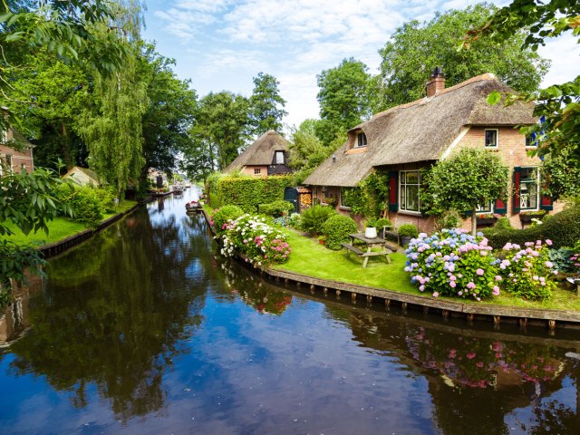Flowers and thatched-roof homes along canal in Giethoorn, The Netherlands