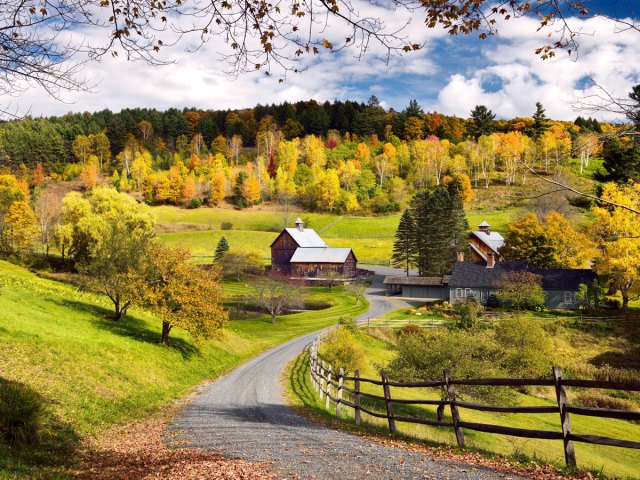 Dirt road winding down hill to farm surrounded by fall foliage in Woodstock, Vermont