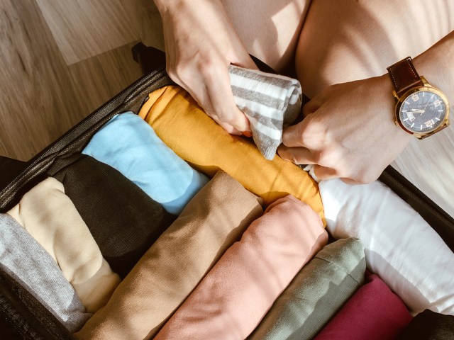 Close-up shot of traveler rolling clothes and placing them in suitcase