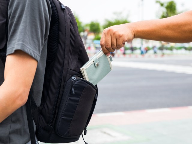 Close-up image of person on street placing wallet into companion's backpack