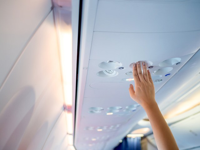 Close-up shot of person holding hand up to passenger service unit above airplane seat