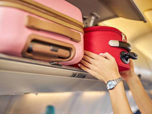 Close-up image of passenger placing suitcase in aircraft overhead bin