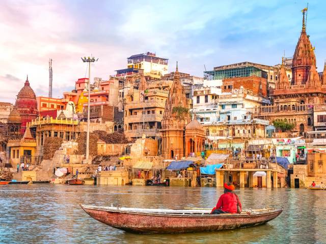 Person on small boat overlooking densely packed buildings on hillside in Varanasi, India