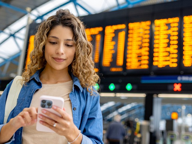 Traveler checking phone with airport departures board in background