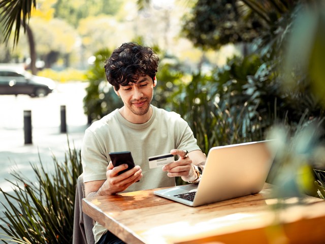 Man sitting at outdoor table with laptop and holding credit card and phone