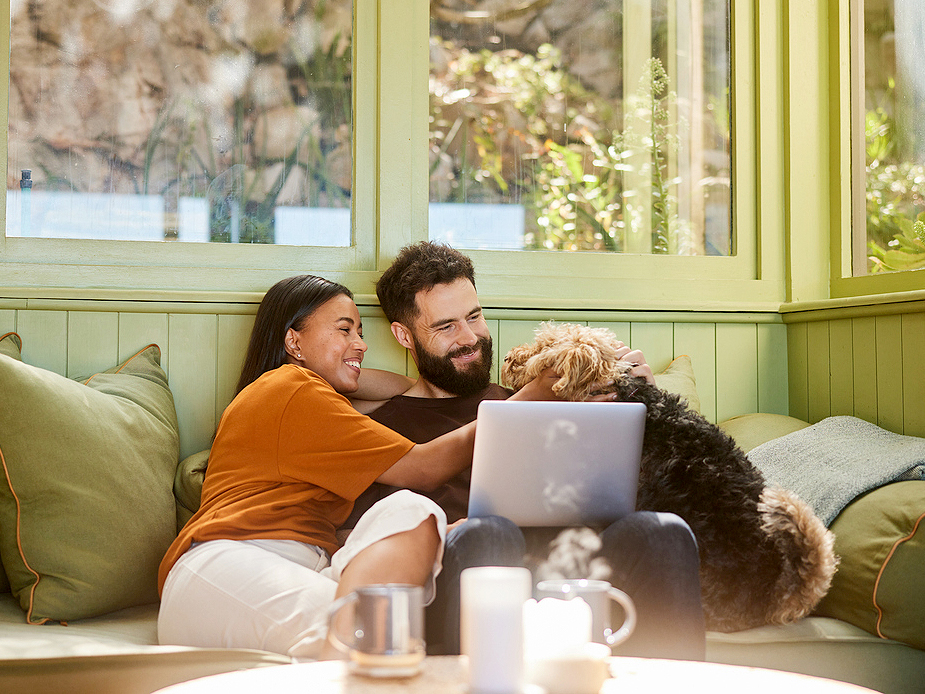 Couple with dog on couch looking at laptop