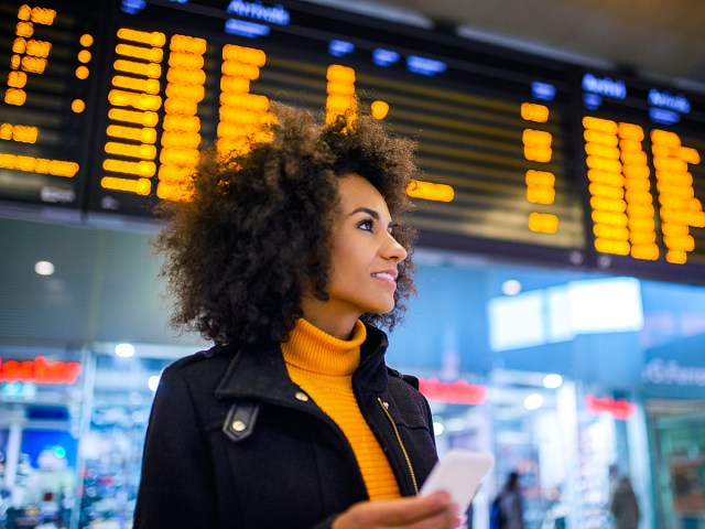 Traveler at airport with blurry departures and arrivals board behind her