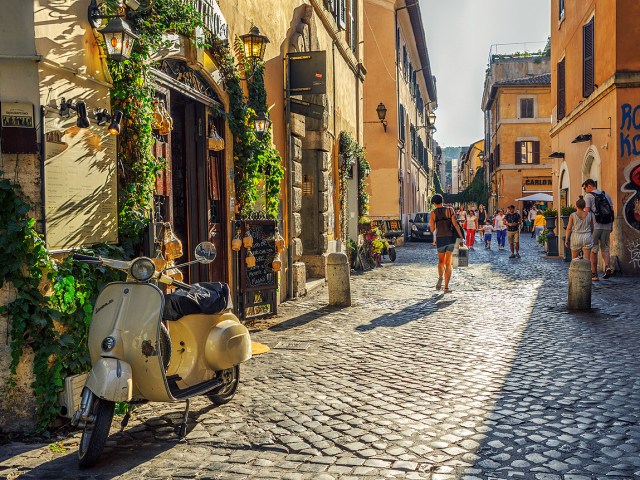Pedestrians and motorbike on narrow cobblestone street in Rome, Italy