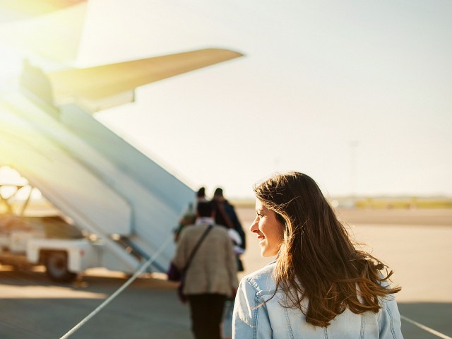 Passenger looking away from camera as she lines up to board airplane through air stairs on airport tarmac