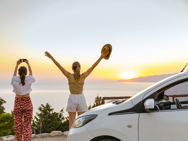 Two women standing next to car looking at ocean