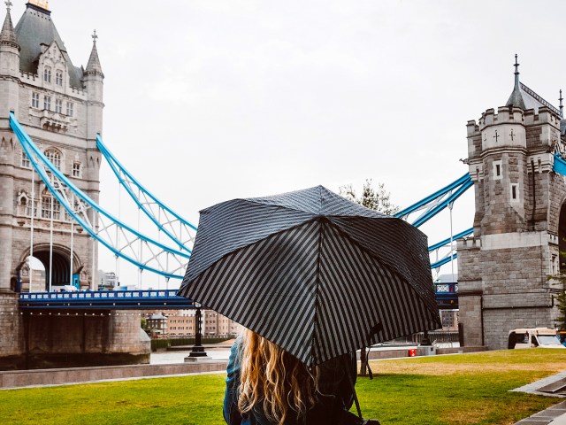 Woman with back to camera holding umbrella and looking at Tower Bridge in London, England