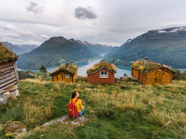 Traveler sitting on moss-covered hillside with small homes overlooking fjord in New Zealand