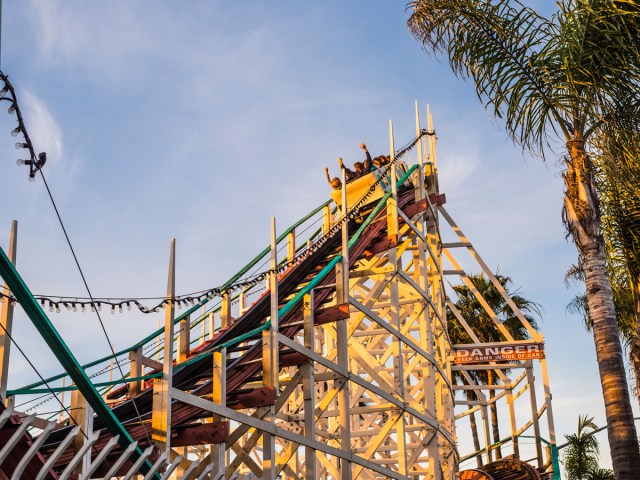 Riders throwing hands in the air at top of roller coaster 