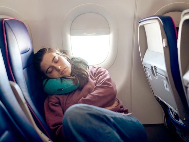 Woman in airplane seat reclining with neck pillow