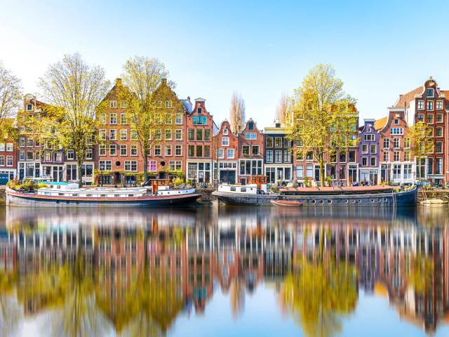 Row houses and boats with reflection on canal in Amsterdam, the Netherlands