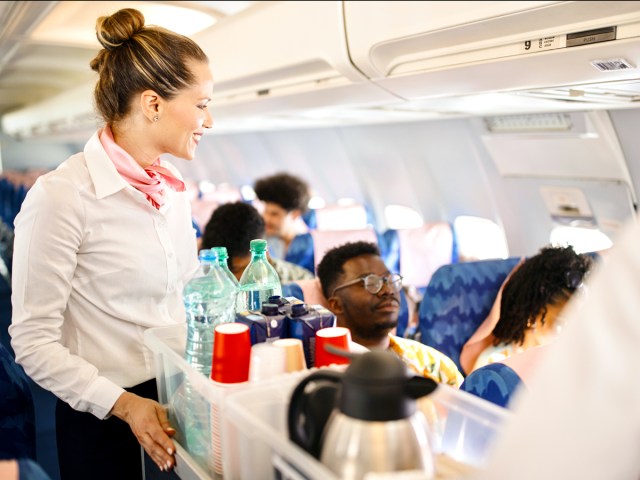 Flight attendant rolling beverage cart through airplane cabin
