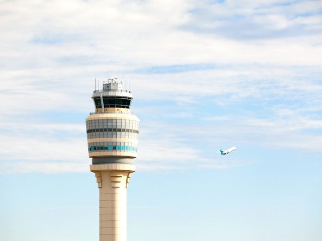View of airport control tower with airplane taking off in background