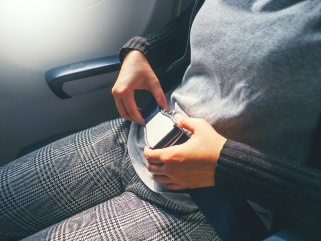 Close-up image of passenger on airplane fastening seat belt in seat