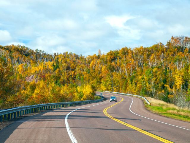 Lone car next driving by fall foliage along the North Shore Scenic Drive in Minnesota