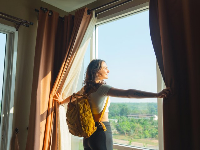 Traveler pulling curtains open to look outside hotel room window
