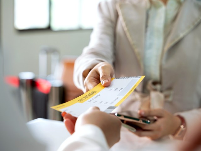 Close-up image of passenger handing boarding pass to agent at airport