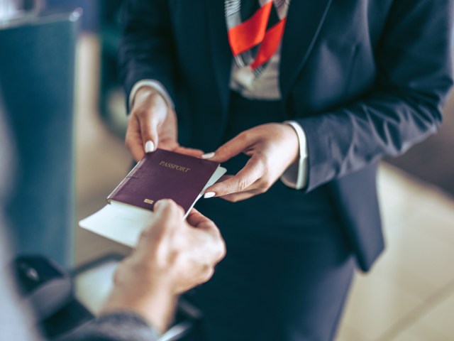 Zoomed-in image of person handing passport and boarding pass to airport agent