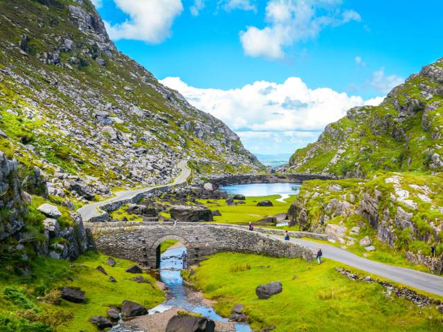 Stone arch bridge over small river in rocky green valley in Ireland
