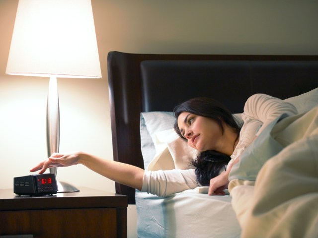 Woman in hotel room bed turning off alarm clock