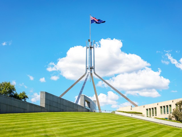 Australian flag flying over government building on grassy hill in Canberra