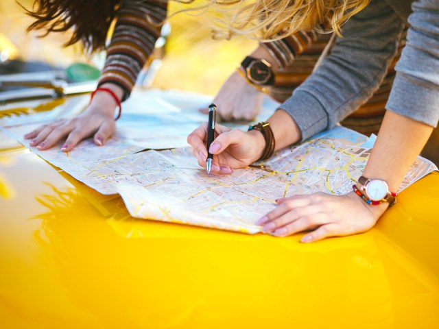 Close-up image of two people writing on map on yellow hood of car