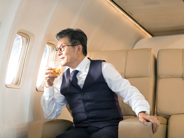 Passenger in first class holding drink and looking out of airplane window