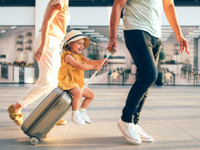 Couple with small child on rolling suitcase in airport