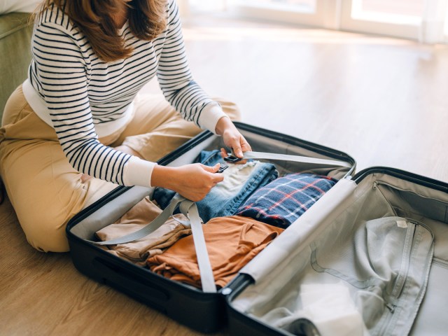 Close-up image of traveler packing suitcase while sitting on floor