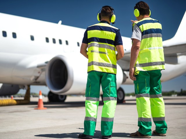 Two ramp marshals dressed in bright safety gear looking at aircraft on airport tarmac