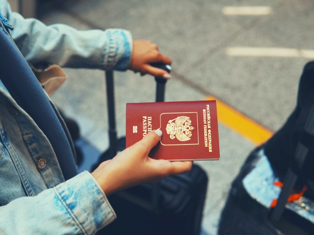Close-up of traveler holding red passport in one hand and luggage handle in the other