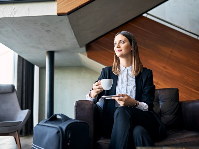 Business traveler holding cup of coffee next luggage in airport lounge