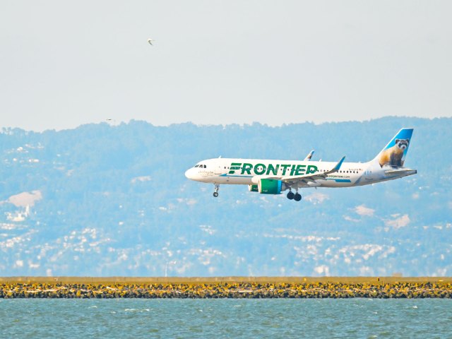 Frontier Airlines landing on airport runway next to body of water