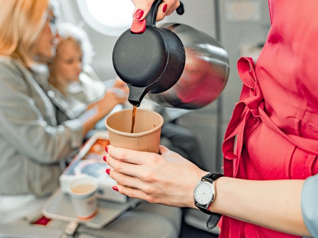 Close-up image of flight attendant pouring coffee in airplane aisle next to seated passengers