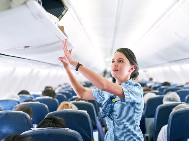 Flight attendant closing overhead bin on airplane