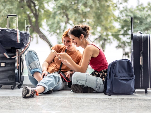 Pair of travelers sitting on floor looking at phone next to their luggage