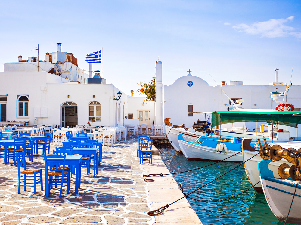 Blue and white patio chairs and tables alongside marina in Paros, Greece