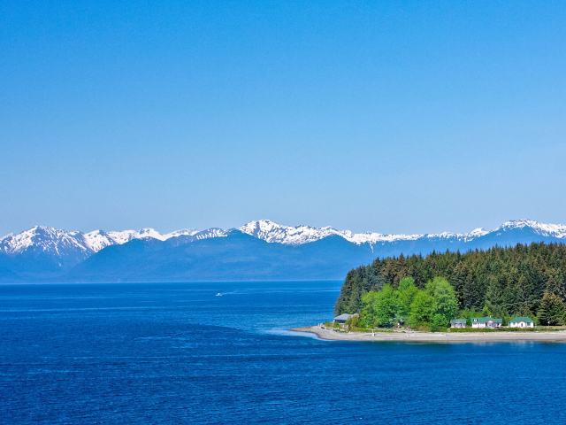 Waterfront homes and forest on Chichagof Island, seen from a distance with snow-capped peaks in the background