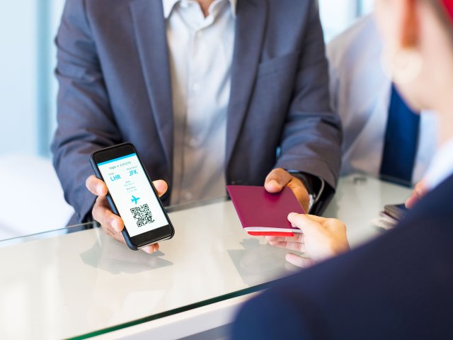 Passenger handing over passport and showing boarding pass on mobile phone to airport check-in agent